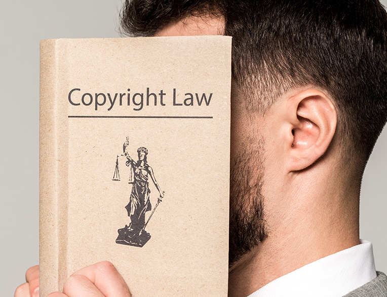 Male lawyer with head covered by book titled, "Copyright Law." Man is ignoring the viewer.